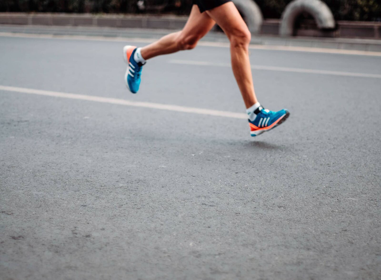 Close-up of a runner's legs and bright blue running shoes on tarmac