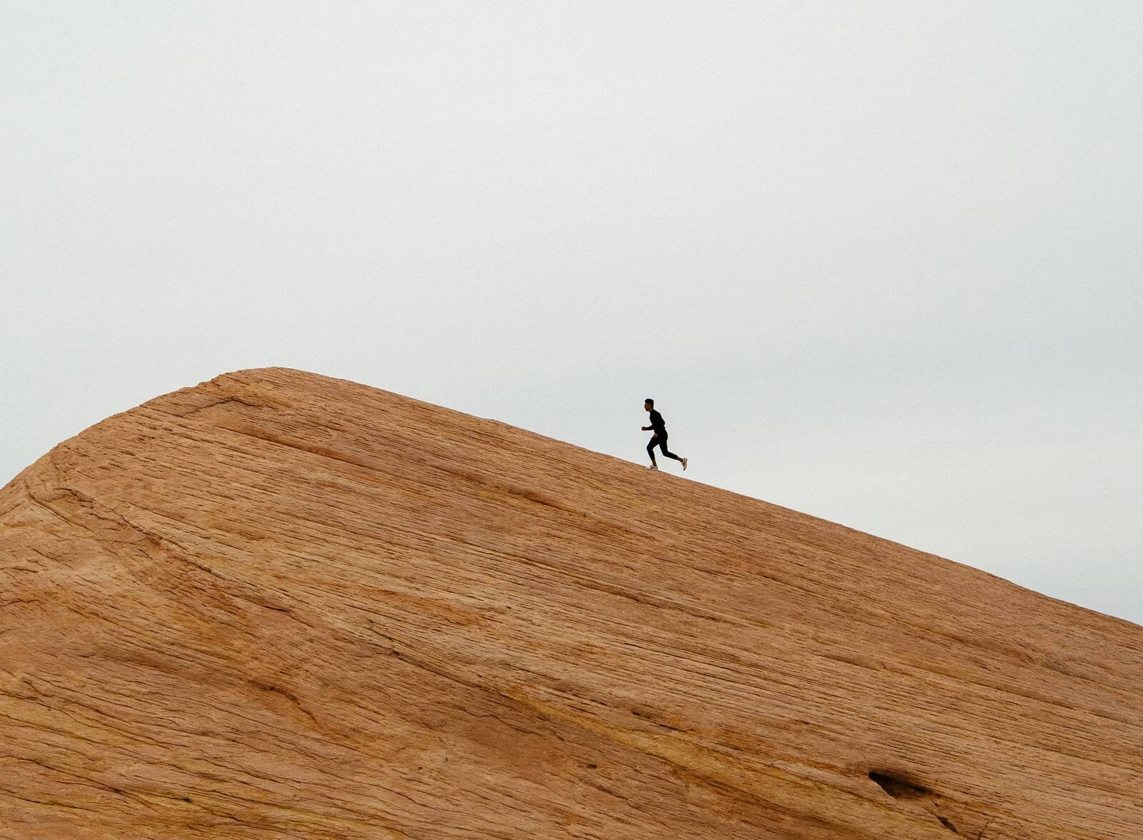 A tiny runner silhouetted on top of a huge sandstone dome